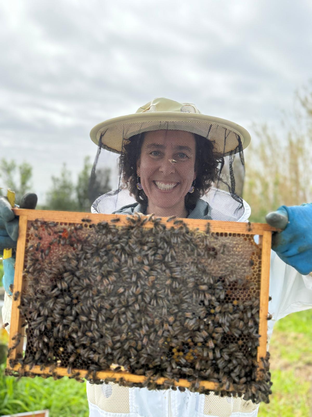 Carolina holding up a frame full of bees, smiling